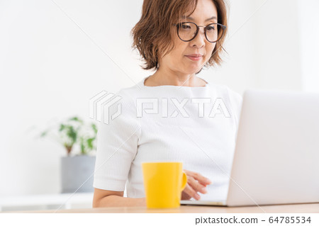 看便攜式計算機的資深婦女在屋子裡 看便攜式計算機的資深婦女在屋子裡 64785534