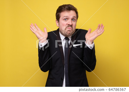 Young funny businessman in suit being uncertain Young funny businessman in suit being uncertain 64786367