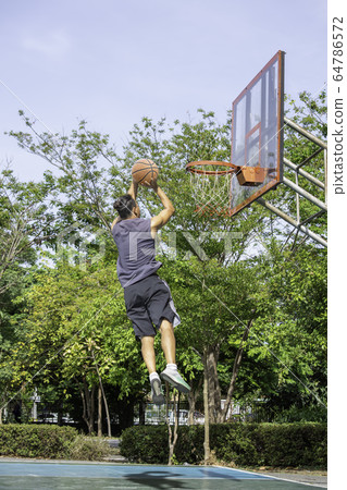 Basketball in hand man jumping Throw a basketball hoop Background tree in park. Basketball in hand man jumping Throw a basketball hoop Background tree in park. 64786572