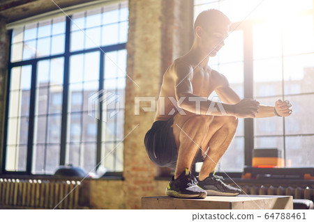 Side view of jumping sportsman on wooden box in gym against background of large window 64788461