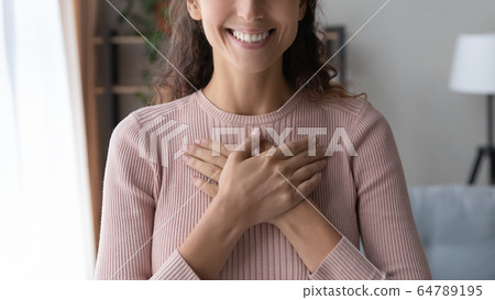 Close up happy sincere female holding folded hands on chest. Close up happy sincere female holding folded hands on chest. 64789195