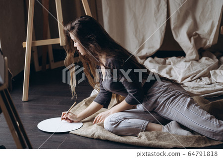 Brunette girl sitting on the floor draws with a brush 64791818