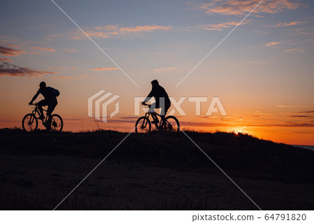 two friends on bikes enjoy a beautiful sunset 64791820