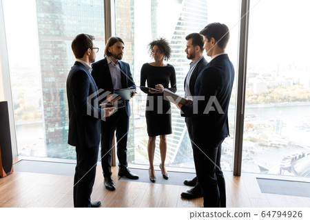 Diverse businesspeople standing in modern office, discussing project Diverse businesspeople standing in modern office, discussing project 64794926