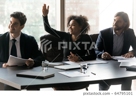 Smiling African American businesswoman raising hand, asking question 64795101