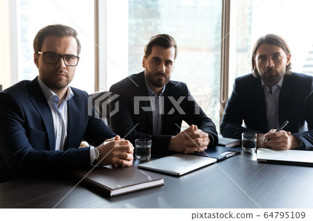 Portrait serious three businessmen employees sitting at table in boardroom 64795109