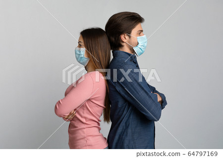 Young woman and man in medical masks standing back to back 64797169