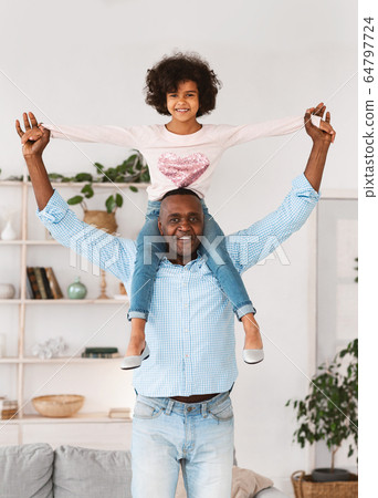 Funny games with granddad. Senior African American man carrying his granddaughter on shoulders at home 64797724