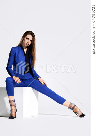 Low angle view of a girl in tulle socks and blue suit sits on white wooden cube in studio Low angle view of a girl in tulle socks and blue suit sits on white wooden cube in studio 64799723