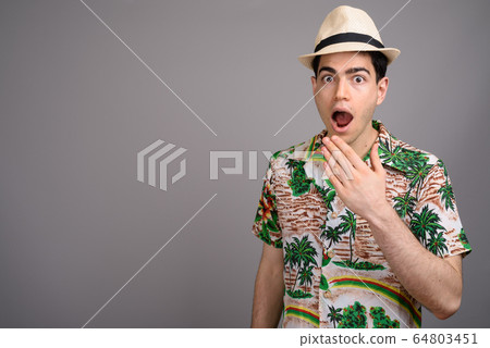 Young handsome tourist man ready for vacation against gray backg Young handsome tourist man ready for vacation against gray backg 64803451
