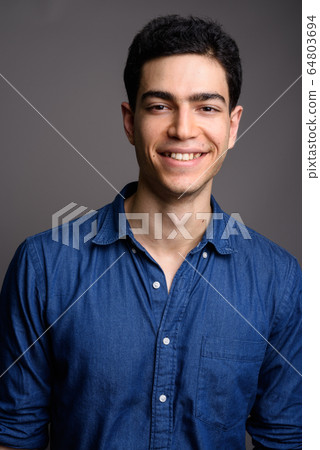 Portrait of young handsome businessman against gray background 64803694