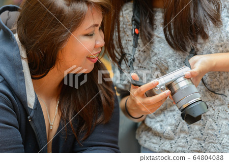 Happy young Asian women as friends checking camera together at the coffee shop outdoors Happy young Asian women as friends checking camera together at the coffee shop outdoors 64804088