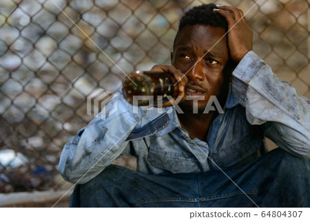 Depressed young homeless African man drinking beer Depressed young homeless African man drinking beer 64804307