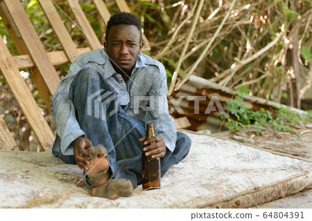 Young homeless African man drinking beer in the streets 64804391