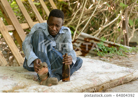 Young homeless African man drinking beer in the streets 64804392