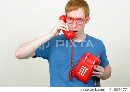 Man with red hair talking on old telephone and looking shocked 64804477
