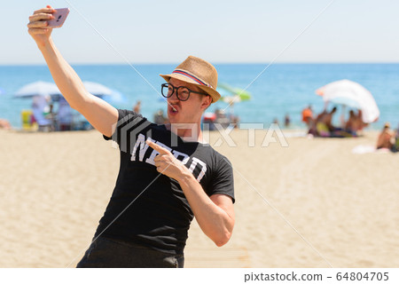 Young nerd tourist man taking selfie at the beach Young nerd tourist man taking selfie at the beach 64804705