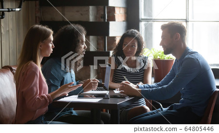 Multiracial colleagues cooperate in coffeehouse working on laptop 64805446