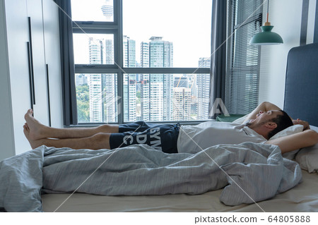 The guy is lying on the bed near the window with The guy is lying on the bed near the window with 64805888