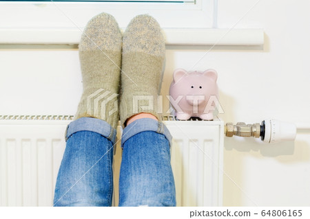 Woman warming up her feet near Piggy Bank On Radiator 64806165
