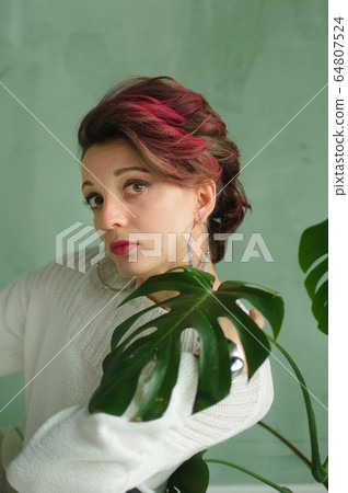 Portrait of a young beautiful woman with perfect smooth skin with a large green tropical leaf. Fashion, beauty, makeup, cosmetics, health, ecology, nature, spa, wellness. 64807524