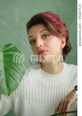 Portrait of a young beautiful woman with perfect smooth skin with a large green tropical leaf. Fashion, beauty, makeup, cosmetics, health, ecology, nature, spa, wellness. 64807525