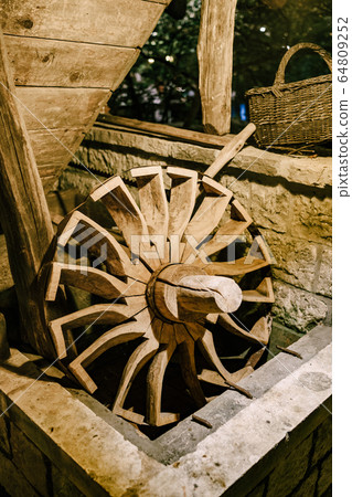 The wheel of a water mill. The old wooden wheel of the water mill is used as an element of decor on the wall. The wheel of a water mill. The old wooden wheel of the water mill is used as an element of decor on the wall. 64809252