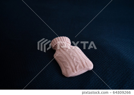Medical hot-water bottle. Medical heating pad in a wool case of pink wool rests on a plaid of blue Medical hot-water bottle. Medical heating pad in a wool case of pink wool rests on a plaid of blue 64809266
