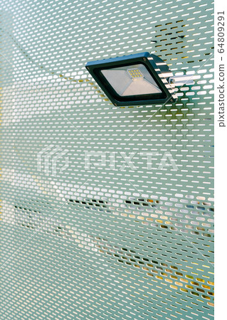 Building LED floodlight. Rectangular floodlight. A small spotlight hangs on a green wall with perforation. Building LED floodlight. Rectangular floodlight. A small spotlight hangs on a green wall with perforation. 64809291