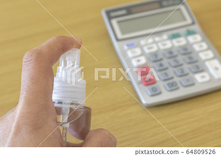 A man disinfects a calculator with a disinfectant spray 64809526