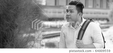 Overweight Asian tourist man travelling with backpack at railway train station Overweight Asian tourist man travelling with backpack at railway train station 64809559