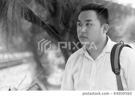 Overweight Asian tourist man with backpack thinking at railway train station 64809560
