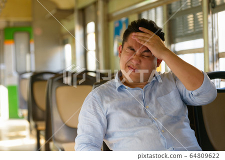 Stressed overweight Asian tourist man feeling hot inside the train Stressed overweight Asian tourist man feeling hot inside the train 64809622