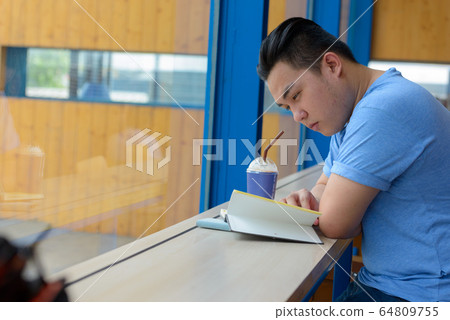 Young handsome overweight Asian man reading book at the coffee shop Young handsome overweight Asian man reading book at the coffee shop 64809755