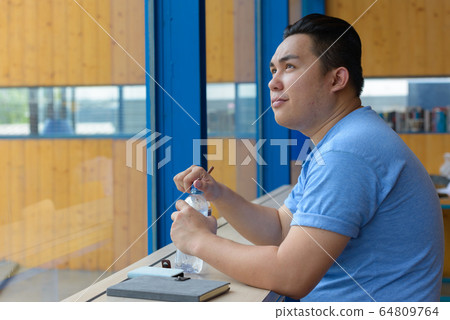 Young overweight Asian man drinking water at the coffee shop Young overweight Asian man drinking water at the coffee shop 64809764