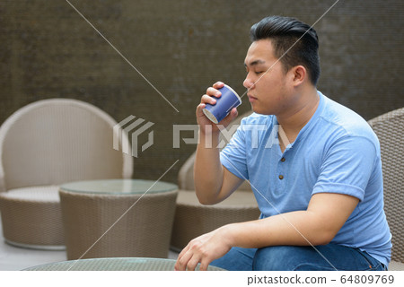 Young overweight Asian man drinking coffee at the coffee shop Young overweight Asian man drinking coffee at the coffee shop 64809769