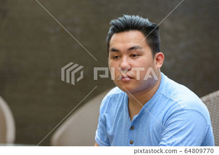 Young overweight Asian man thinking at the coffee shop Young overweight Asian man thinking at the coffee shop 64809770
