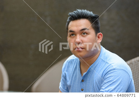 Young overweight Asian man thinking at the coffee shop 64809771