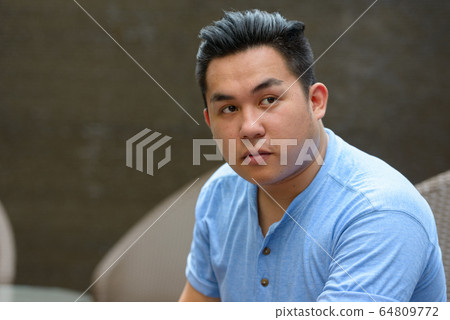 Young overweight Asian man thinking at the coffee shop 64809772