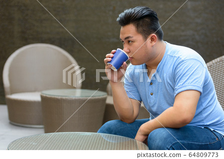 Young overweight Asian man drinking coffee at the coffee shop Young overweight Asian man drinking coffee at the coffee shop 64809773