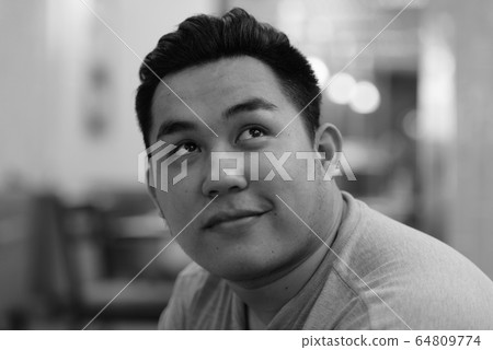 Face of happy young overweight Asian man thinking at the coffee shop Face of happy young overweight Asian man thinking at the coffee shop 64809774