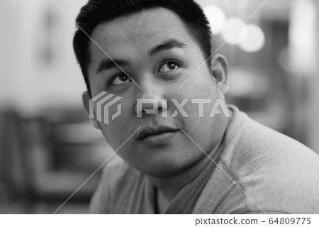 Face of young overweight Asian man thinking at the coffee shop Face of young overweight Asian man thinking at the coffee shop 64809775