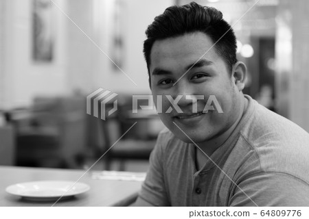 Face of happy young overweight Asian man smiling at the coffee shop Face of happy young overweight Asian man smiling at the coffee shop 64809776