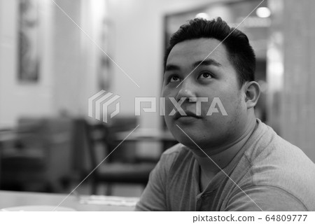 Face of young overweight Asian man thinking at the coffee shop Face of young overweight Asian man thinking at the coffee shop 64809777