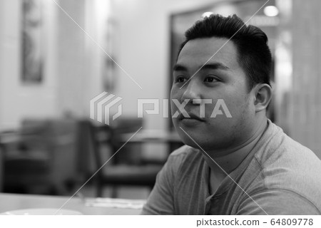 Face of young overweight Asian man thinking at the coffee shop Face of young overweight Asian man thinking at the coffee shop 64809778