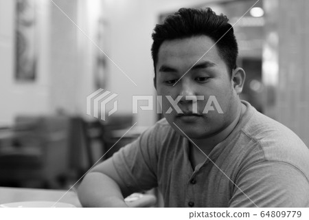 Stressed young overweight Asian man thinking at the coffee shop 64809779