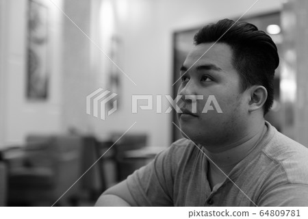Face of young overweight Asian man thinking at the coffee shop Face of young overweight Asian man thinking at the coffee shop 64809781