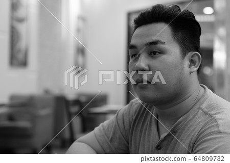 Face of young overweight Asian man thinking at the coffee shop Face of young overweight Asian man thinking at the coffee shop 64809782