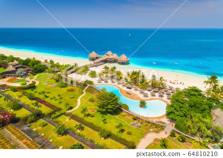Aerial view of beautiful hotel on the sea, pool, umbrellas and green palm trees on the sandy beach Aerial view of beautiful hotel on the sea, pool, umbrellas and green palm trees on the sandy beach 64810210