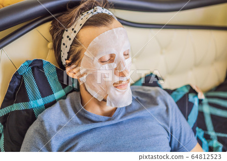 Young man doing facial mask sheet. Beauty and Skin Care Concept 64812523